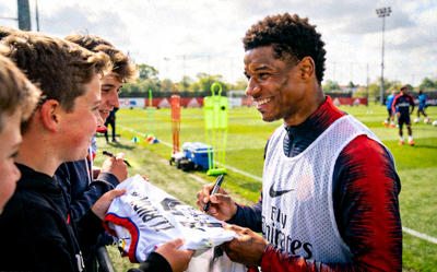 足球巨星在训练场边与球迷亲切互动，笑容满面